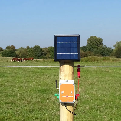 LUDA FenceAlarm med solpanel monteret på en pæl til overvågning af hegnsspænding på en græsmark.