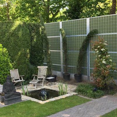 En hyggelig have med buske og en lille fiskedam afskærmet fra nabostøj med et Noistop® Steel støjhegn fra Poda Hegn