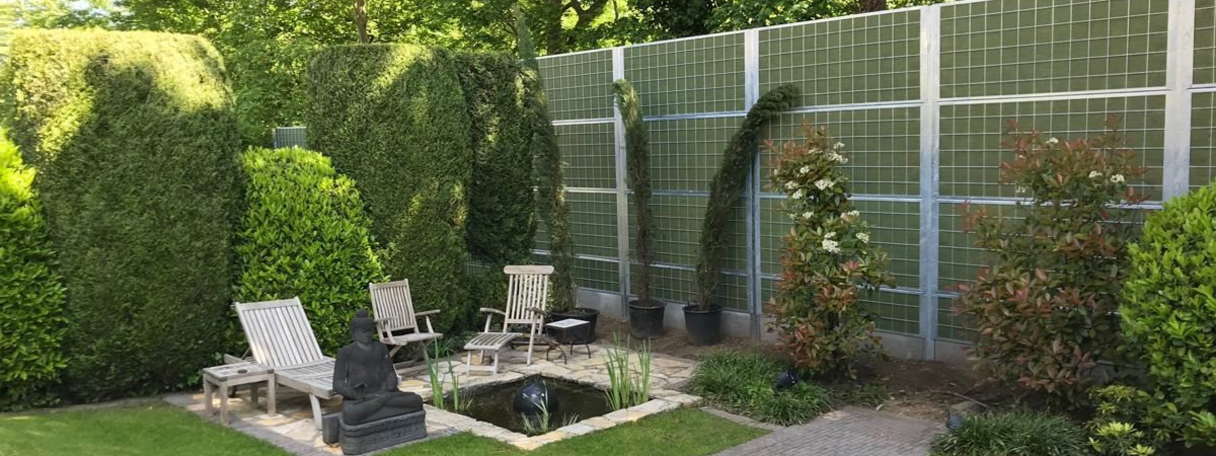 En hyggelig have med buske og en lille fiskedam afskærmet fra nabostøj med et Noistop® Steel støjhegn fra Poda Hegn