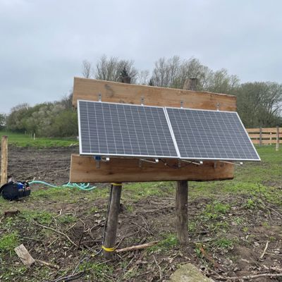 Soldrevet markpumpe med solpaneler monteret på en trækonstruktion i en græsfold
