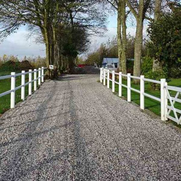 En indkørsel med et hvidt lægtehegn på begge sider fører op til en landejendom.