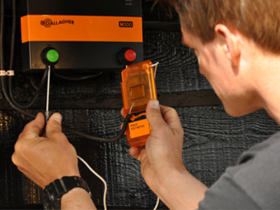 Montør der tjekker strømmen på en hegnsspændingsgiver med et voltmeter.