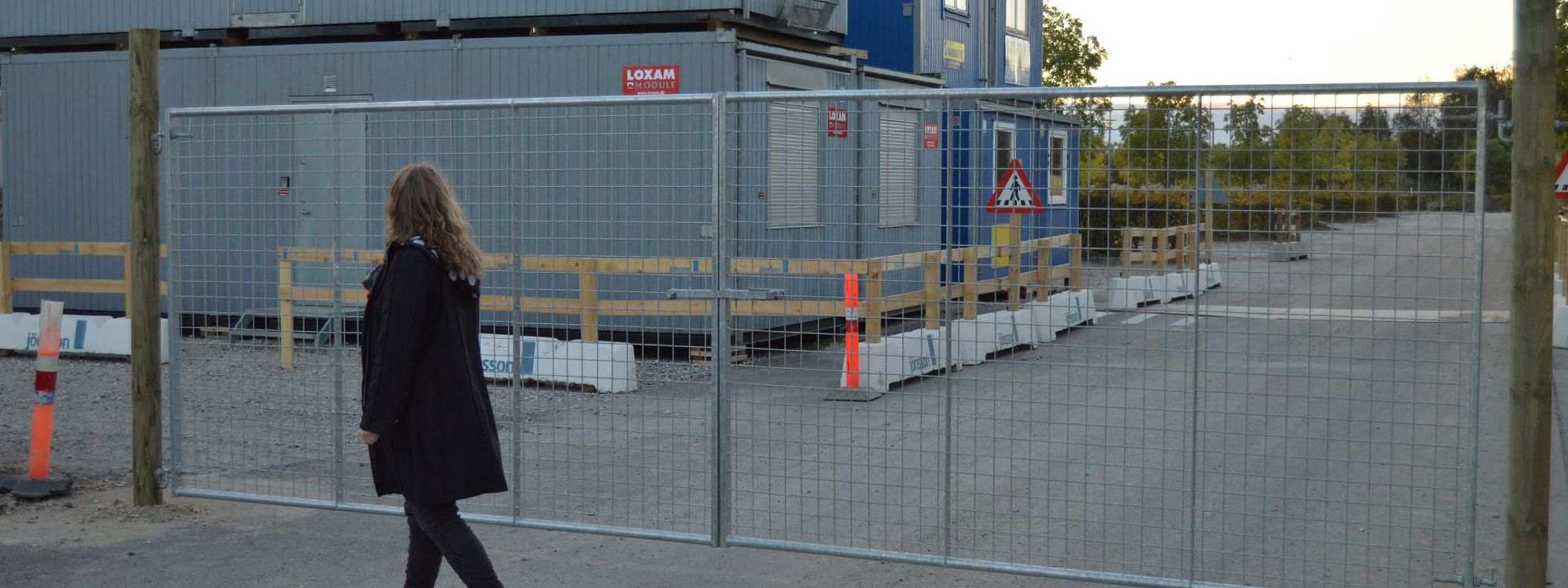 En dame går foran en letvægtslåge, der er monteret ved en byggeplads