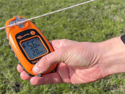 En hånd holder en hegns doktor, der måler strømstyrken og spændingen på et elektrisk hegn.