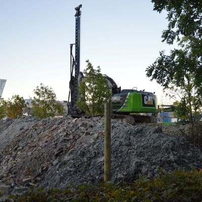 En grøn CAT maskine holder parkeret ovenpå en grusbunke. Maskinen er sikret med et byggepladshegn