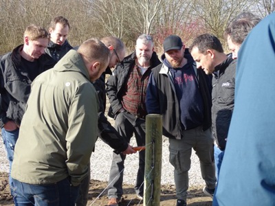 Poda-centre samles om en hegnspæl under en træningssession, hvor de lærer at bruge en måler til elektriske hegn.