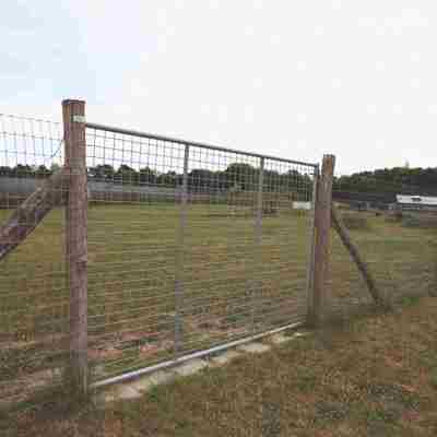 En høj stållåge giver adgang til en løbegård til hunde.