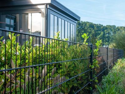 I en have er der monteret panelhegn med grønne planter på begge sider