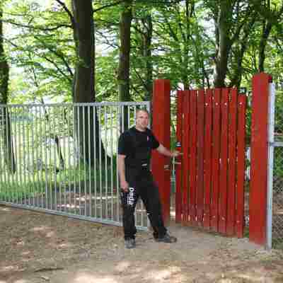 En mand står foran en rød trælåge, der fører ind til en dyrehave. Ved siden af lågen ses en port i stål.