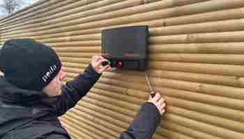 En montør er i gang med at sætte en strømgiver op på et hegn