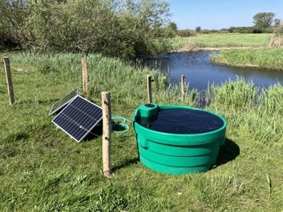 soldrevet markpumpe der står ud til en å