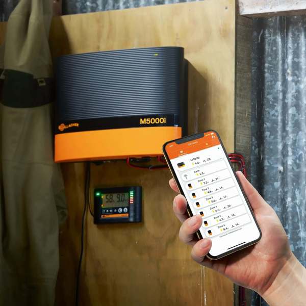 Strømgiver M5000 der hænger på en væg, hvor den tilhørende telefon app bliver vist frem