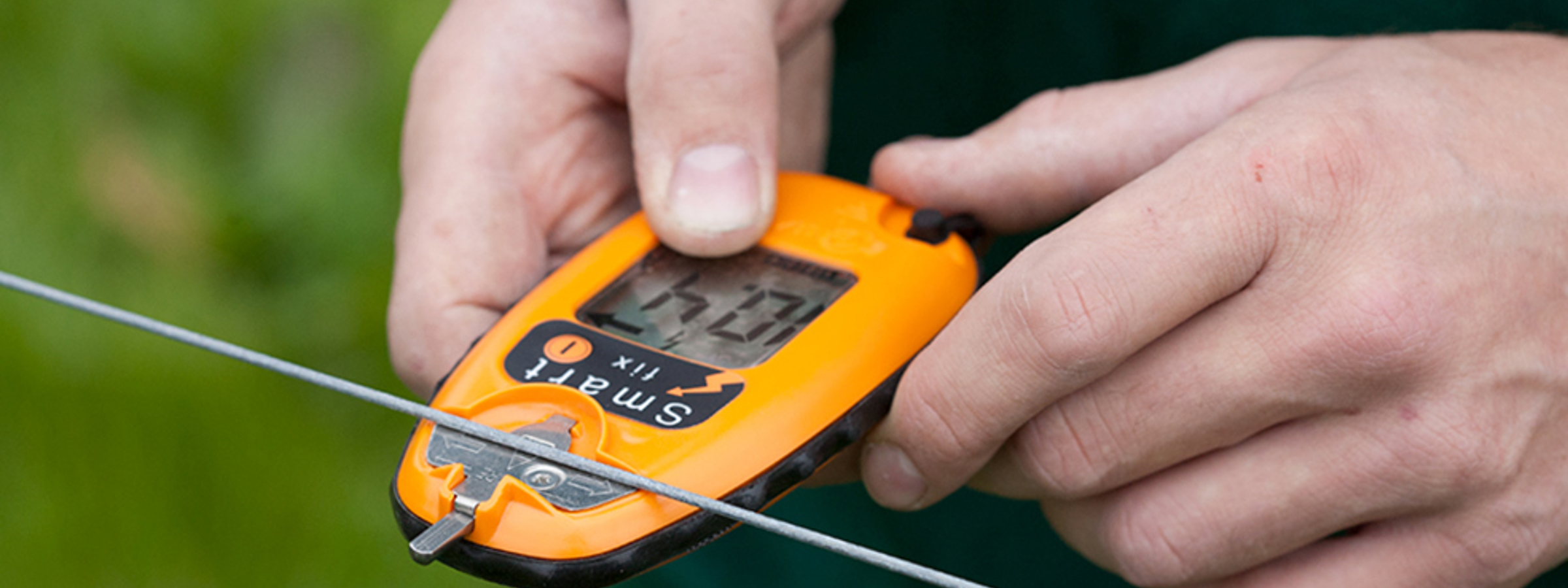 En person bruger en hegns doktor til at måle spændingen på et elektrisk hegn.