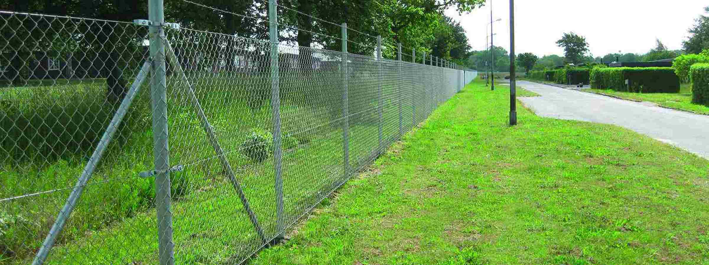 Et højt flethegn med to tråde monteret ovenpå beskytter et grønt område