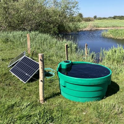 Soldrevet markpumpe med solpanel og vandkar ved en å på en græsmark