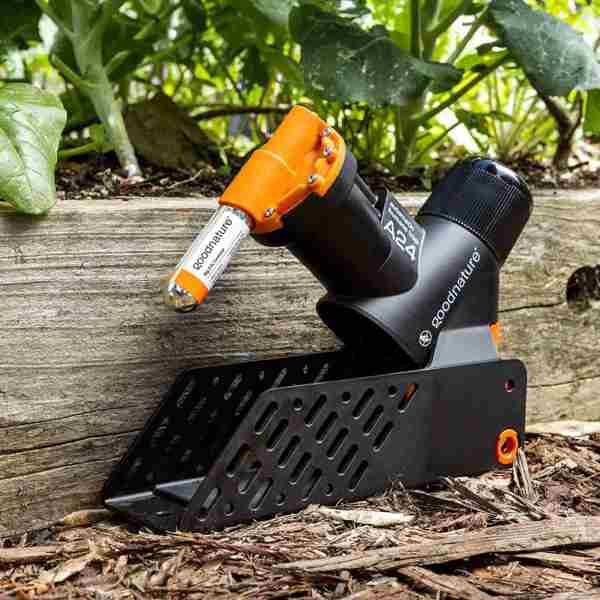 Goodnature rotte- og musefælde opsat i en have ved en træafgrænsning.