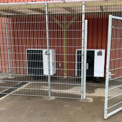 Inde bagved et gråt panelhegn står der to varmepumper