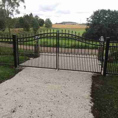 I forlængelse af et hegn, er der monteret en sort smedejernslåge i samme design som hegnet