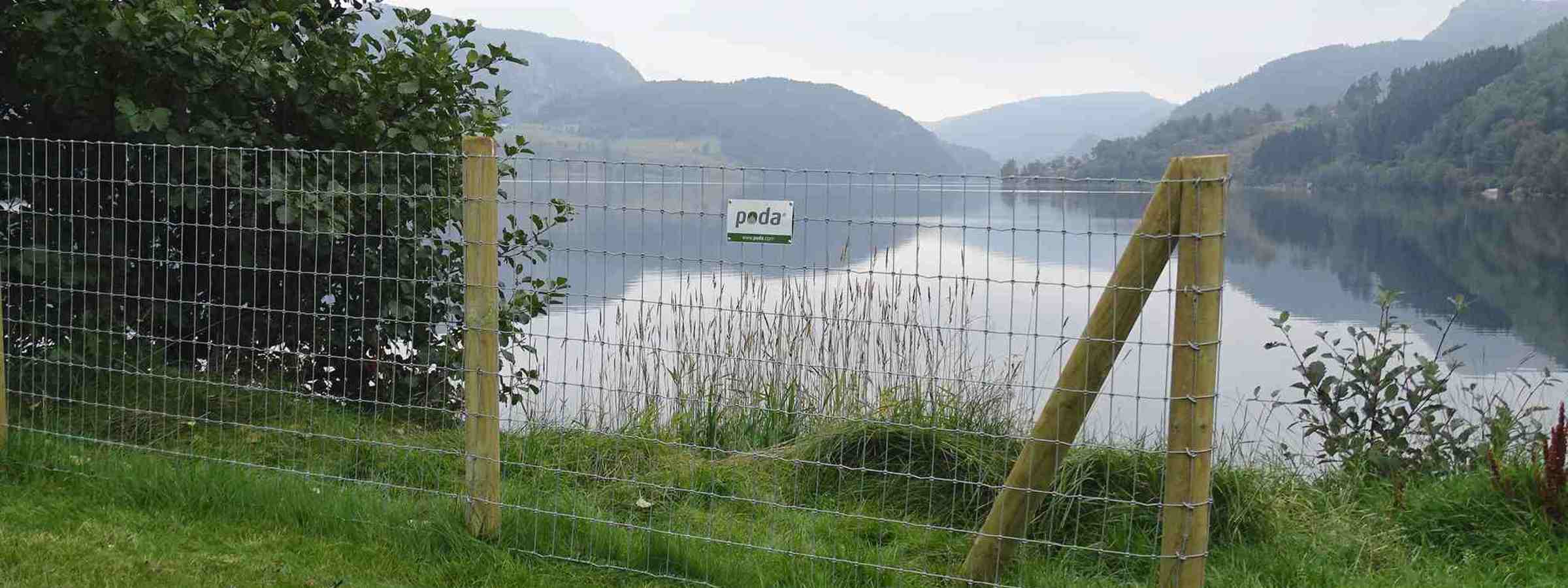 I forgrunden er en afsluttende pæl på et Multinet. I baggrunden er der en sø.