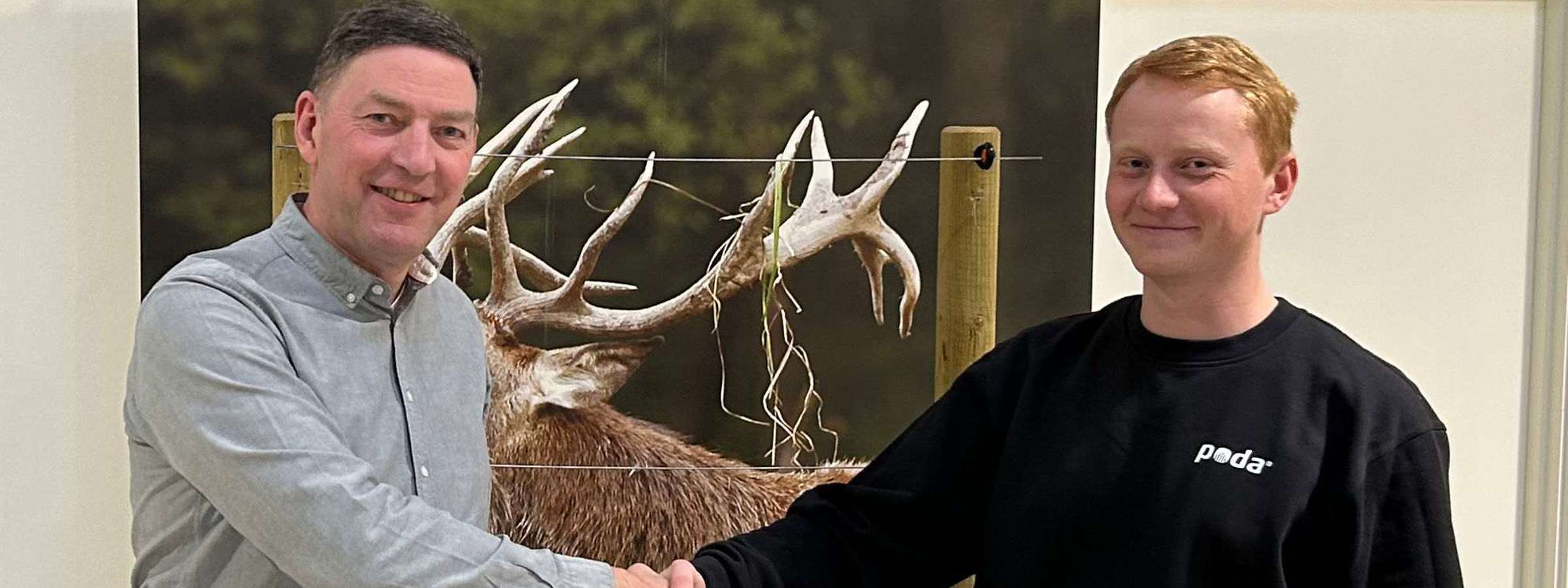 Poda-direktør Peter giver hånd til Sofus fra Poda Hegn Ringe, foran et banner med kronhjort og elhegn.