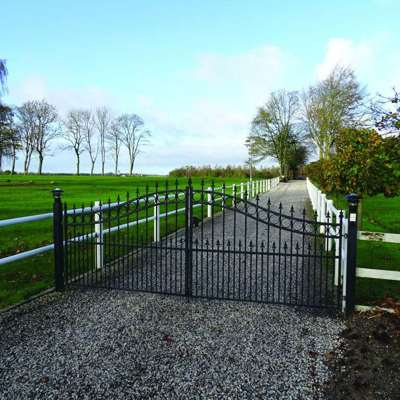 Omringet af et hvidt lægtehegn er en sort smedejernslåge monteret i starten af en indkørsel