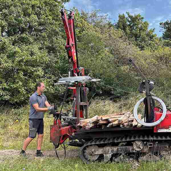 En montør er i gang med at rulle tråd ud til et elektrisk hegn med en specialbygget maskine i et grønt og skovrigt område.