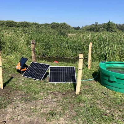 Soldrevet markpumpe med solpaneler og drikkekar ved et indhegnet vandløb