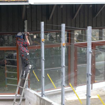 En mand monterer eltråde på toppen af et højt hegn i en zoo.