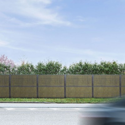 Noistop Essential støjhegn med antracitgrå ramme, omgivet af grøn beplantning, med en fodgænger og en forbipasserende bil i forgrunden.