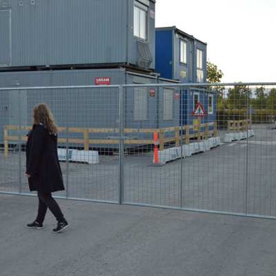 En dame går foran en letvægtslåge, der er monteret ved en byggeplads