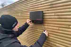 En montør er i gang med at sætte en strømgiver op på et hegn